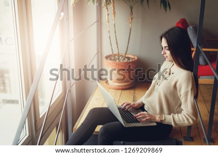 Pretty brunette woman do her work at cafe, wear glasses and chat in laptop near the window. - Image