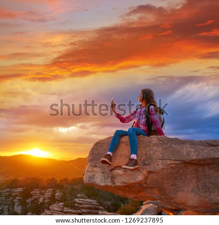 Hiker teen girl selfie smartphone on peak of mountain at sunset