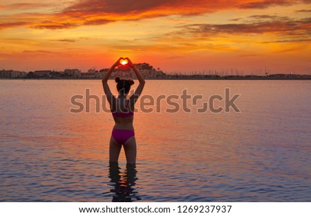 Girl silhouette at sunset heart shape in hands fingers on the beach