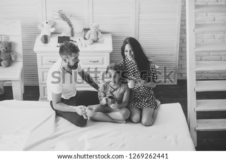 Loving family and cozy home concept. Family with cheerful and happy faces indoors. Man, woman and cute child smile and hold colorful cups. Mother, father and daughter with tea cups in apartment.