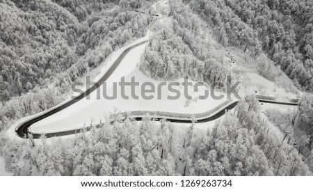 The black road in the snow-covered forest. Snow in the mountains, aerial photography with drone. Trees in snow. Rise, up, lifting, moving.