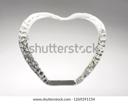 Beautiful and original look and background on an interesting, creative and designer glass and transparent gift and element, pendant, pedestal in the form and heart shape on a gray background.