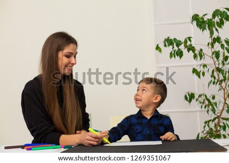 female teacher teaches a little boy to draw at the table