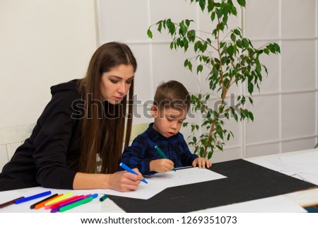 female teacher teaches a little boy to draw at the table