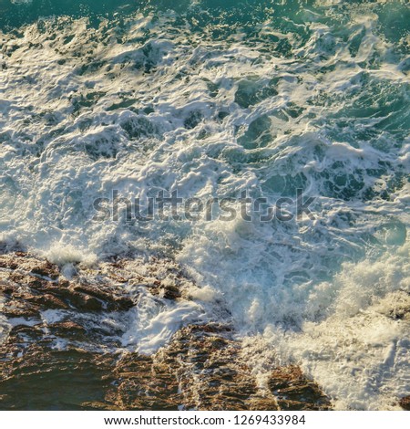 Beautiful green and blue sea water with white foam from the waves crashing on the rocks

