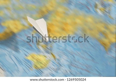 A small paper plane flies over a blurred abstract geographical map of the world. concept of air travel, travel, mail, communication.