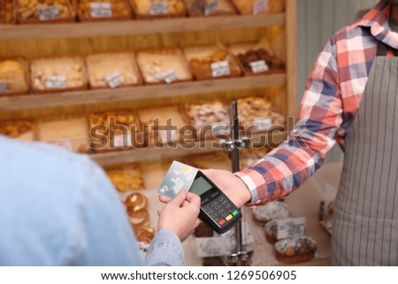 Woman using credit card for terminal payment in bakery, closeup. Space for text