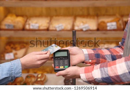 Woman using credit card for terminal payment in bakery, closeup