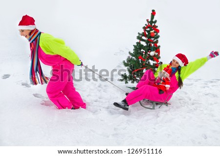 Girlfriend pulling Santa girl on a sled at snow