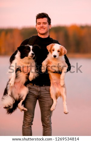 happy guy in black with two funny border collie dog on his hands . autumn yellow forest and lake on background
