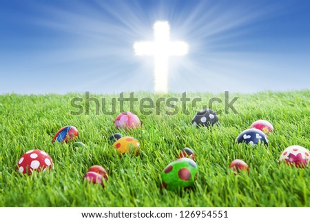 Picture of colorful easter eggs laying on the grass with a bright Cross
