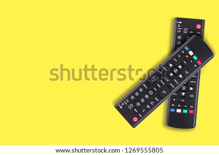 Pair of black plastic remote controls for different multimedia devices on yellow background with copy space for your text. Top view