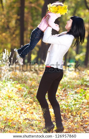 beautiful young mother holding her daughter in a wreath of maple leaves
