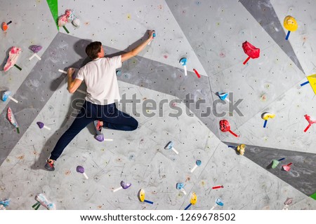 Rock climber man hanging on a bouldering climbing wall, inside on colored hooks Royalty-Free Stock Photo #1269678502