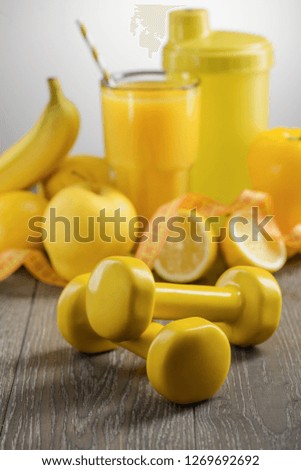 Yellow dumbbells and food, selective focus. Drinking smoothie made of fresh ingredients and doing fitness routine.