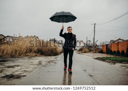 Business man standing in rain with an umbrella. Financial safety. Raining day in city park view, risk and crisis concept.