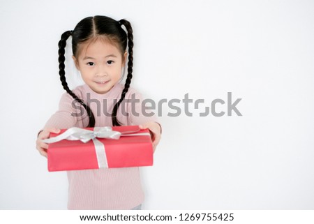 Asian kid girl holding a White ribbon gift red box tied. It is a joy to celebrate the holidays, such as Valentine's Day Christmas and Happy New Year. Concept Universal Children’s Day