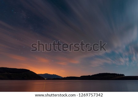 Beautiful moon set on the lake with blue and orange clouds. Night landscape. 