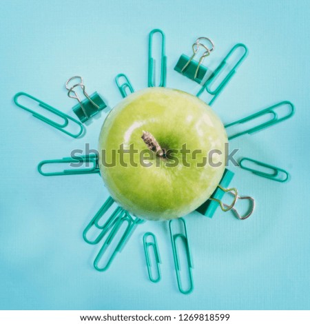 Green apple surrounded by a sunburst of paper clips on a cyan background