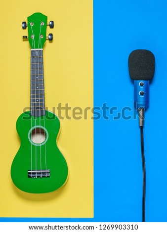 Ukulele and microphone with wires on blue and yellow background. The view from the top.