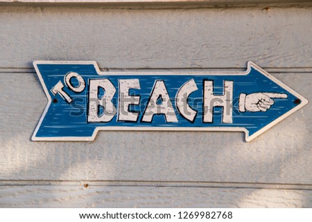 Blue arrow shaped sign with white letters saying to beach with a hand icon pointing in the arrow's direction