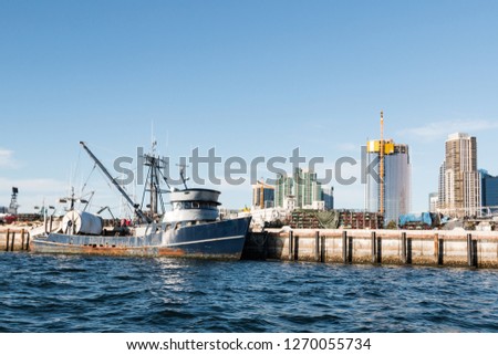 A fishing boat docked at a pier along the Embarcadero in the San Diego, California Harbor, with the downtown skyline in the background.