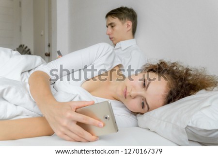 Couple ignoring each other and looking at smartphone on the bed.