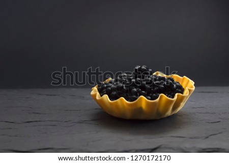 A photo of seafood. Black sturgeon caviar in a tartlet on the dark stone background with copyspace, place for text. Delicatessen and gourmet food. Selective soft focus