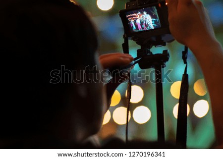 Blurred motion man using the camera with tripod with sparkling bokeh lights in background. Candid portrait from back of man taking the picture