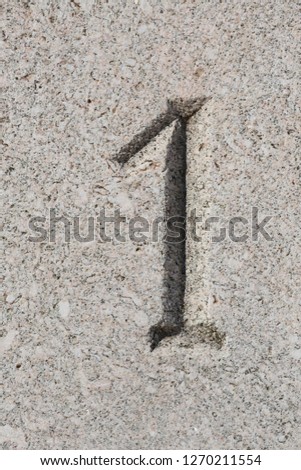 Close up outdoor view of number one engraved in grey stone. Gray textured surface with the sign 1. Abstract picture with a decorative numero.