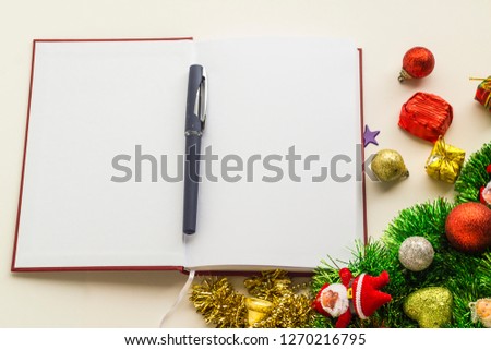 A red hard cover agenda,calendar notebook and a pen,opened near with christmas ornaments on the white surface