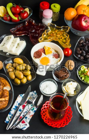 Traditional Turkish Breakfast on the black surface with sausage and egg on the middle of frame.
