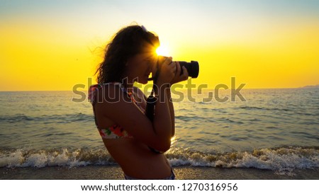 Tourist taking photograph of beach sunset. Girl photographer taking photos using DSLR mirrorless camera