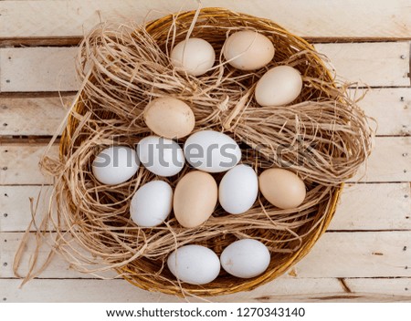 Fresh eggs in a basket with hay on a wooden background.