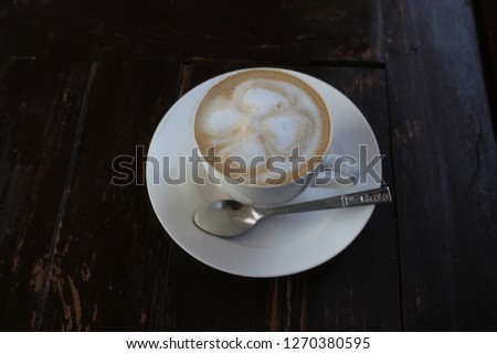 White hot coffee cup with flower shape on top. It is placed on an old white wooden table.