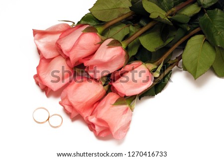Wedding rings and a bouquet of pink roses on a white background top view