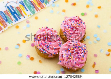 High angle shot of three strawberry cupcakes with sprinkles and icing and happy birthday inscribed in background.