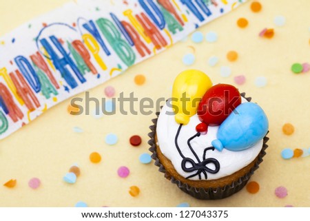 Close-up shot of a cupcake with colorful balloons shape and happy birthday inscribed in background.