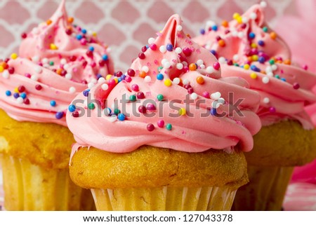 A close-up shot of three cupcakes on pink covered in sprinkles and icing.
