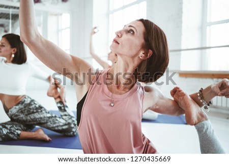 Close-up view on strong healthy woman practicing yoga exerciese on fitness mat in white sport class. Adult fit female doing stretching early morning indoor on background people