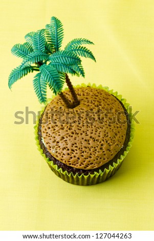 Close-up image of a cupcake with plastic coconut tree miniature over yellow background.