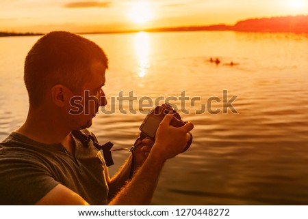 Professional photographer looks through the photos at camera in the evening sunset. Silhouette of man using a camera to take a photo with sunset background.