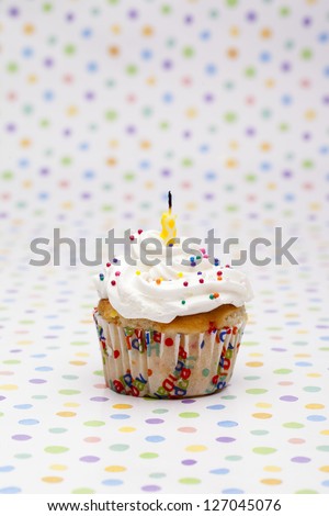 Close-up shot of a cupcake with candle isolated over polka dots background.