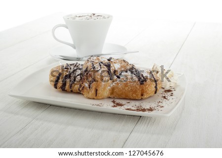 Image of chocolate flavor croissant with hot coffee on the side on a wooden table