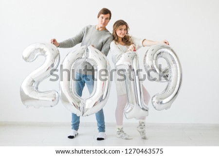 New year, celebration and holidays concept - funny love couple holding sign 2019 made of silver balloons for new year on white background