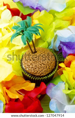 Isolated cupcake with miniature plastic coconut tree surrounded by the colorful flowers of a lei. It's tiki party time!