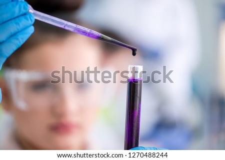 young female student with protective glasses making chemistry experiment in bright laboratory,education and medicine concept