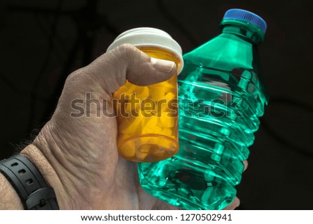Man holds with left hand a bottle of water and a pill bottle