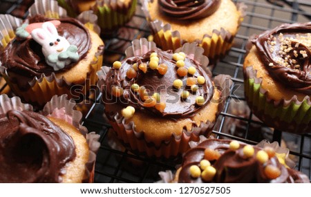 A picture of cupcakes with chocolate frosting, orange sprinkles and a fondant rabbit decoration