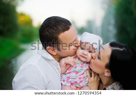 Happy family mother, father, child daughter. Happy young family spending time together outside in green nature. Happy family having fun outdoor. Mom and dad kissing their baby